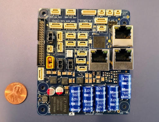 Mission Dock validated PCB with Ethernet ports, isolated serial, supercapacitors, and power connectors; penny for scale
